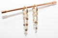 Gold chain earrings hanging on a rod against a white background