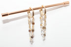 Gold chain earrings hanging on a rod against a white background