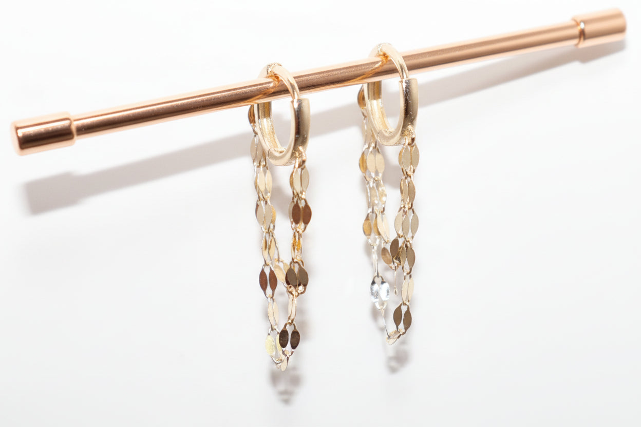 Gold chain earrings hanging on a rod against a white background